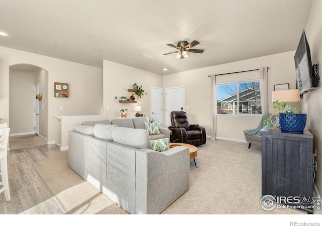 living room with light wood-type flooring, arched walkways, ceiling fan, and baseboards