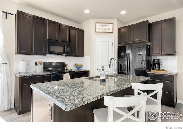 kitchen featuring a sink, a kitchen breakfast bar, light stone countertops, black appliances, and an island with sink