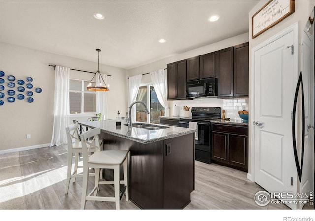 kitchen with stone counters, light wood-style flooring, a sink, black appliances, and tasteful backsplash