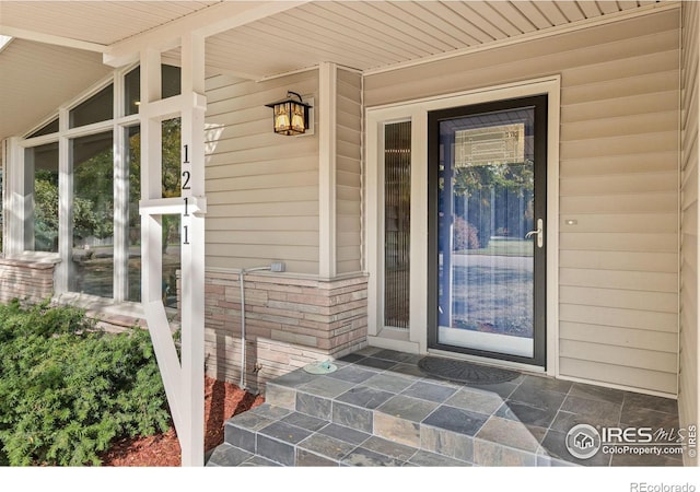 view of exterior entry featuring covered porch and brick siding