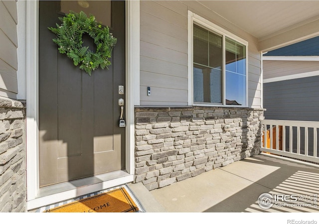 view of exterior entry featuring stone siding and a porch