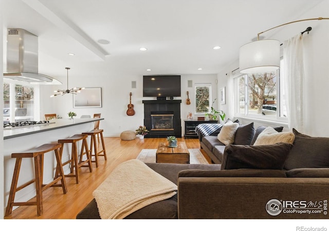 living room featuring light wood-style floors, a tile fireplace, a notable chandelier, and recessed lighting