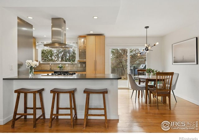 kitchen featuring tasteful backsplash, island range hood, dark countertops, a breakfast bar, and light wood-style floors