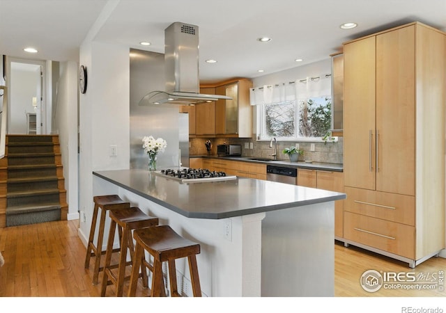 kitchen featuring a breakfast bar, island exhaust hood, dark countertops, decorative backsplash, and appliances with stainless steel finishes