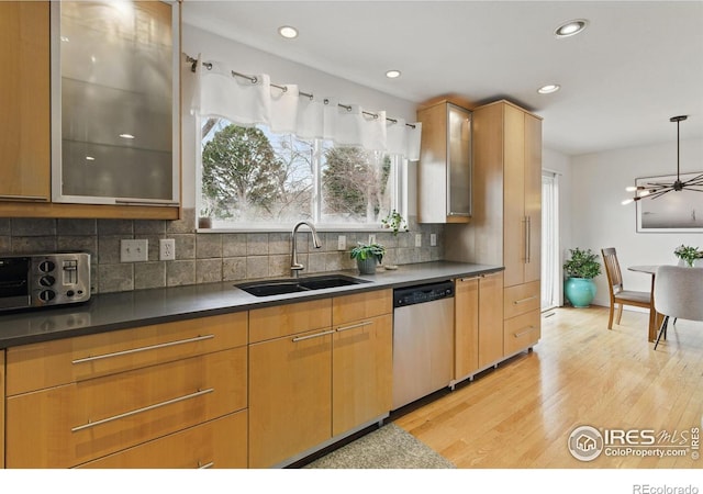 kitchen featuring tasteful backsplash, dishwasher, glass insert cabinets, light wood-style floors, and a sink