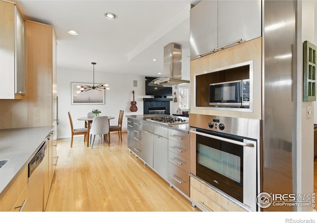 kitchen featuring light brown cabinets, light wood-style flooring, stainless steel countertops, appliances with stainless steel finishes, and island exhaust hood