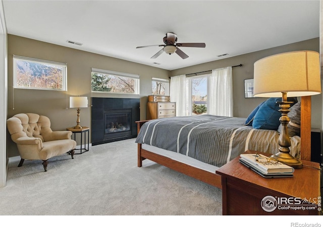 carpeted bedroom with a ceiling fan, visible vents, and a tiled fireplace