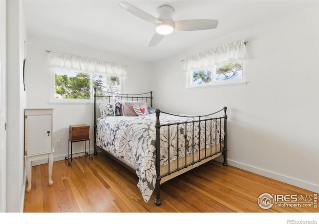 bedroom featuring a ceiling fan, multiple windows, baseboards, and wood finished floors