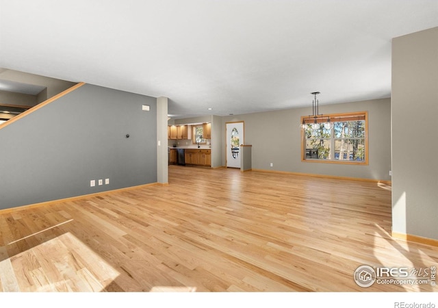 unfurnished living room featuring light wood finished floors, baseboards, and a sink