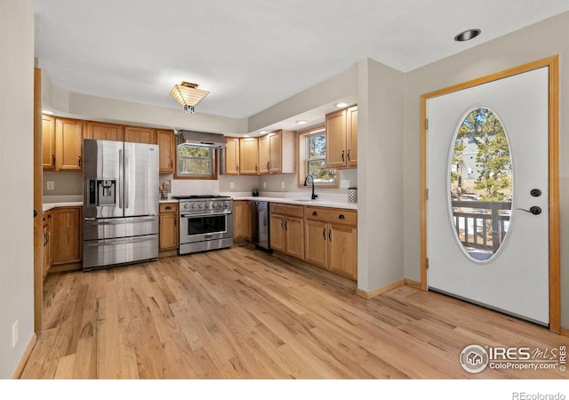 kitchen featuring stainless steel appliances, a sink, light countertops, wall chimney range hood, and light wood finished floors