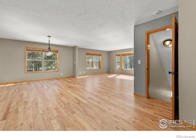 unfurnished living room featuring light wood finished floors, baseboards, and a textured ceiling