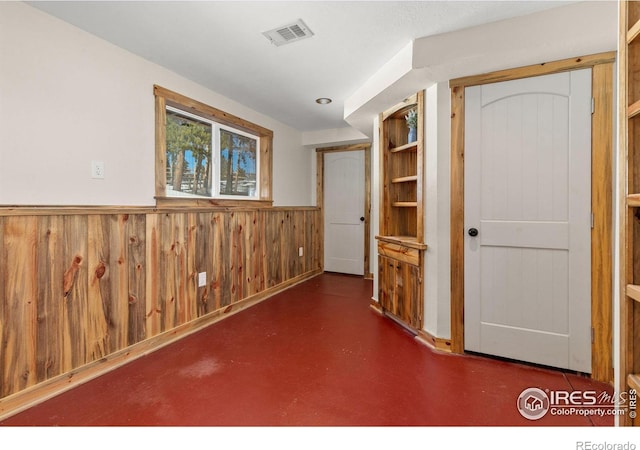 interior space with wooden walls, finished concrete floors, a wainscoted wall, and visible vents