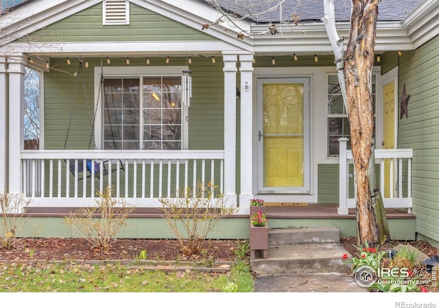 entrance to property with covered porch and a shingled roof