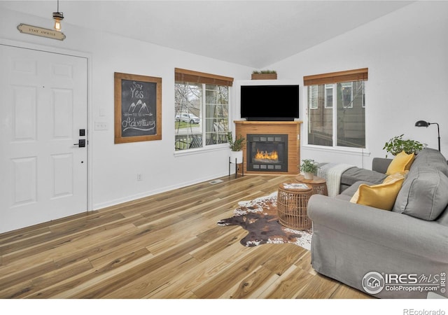 living area with a glass covered fireplace, vaulted ceiling, baseboards, and wood finished floors