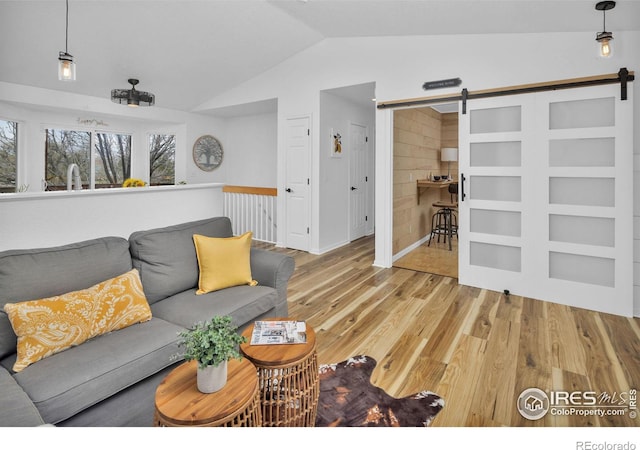 living area featuring vaulted ceiling, a barn door, and wood finished floors