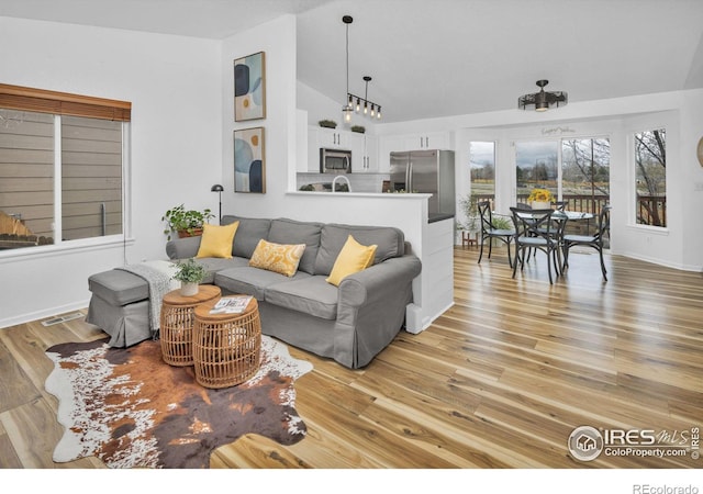 living area with high vaulted ceiling, light wood-type flooring, visible vents, and baseboards