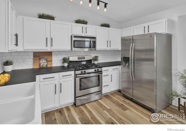 kitchen with dark countertops, lofted ceiling, appliances with stainless steel finishes, light wood-style floors, and white cabinets