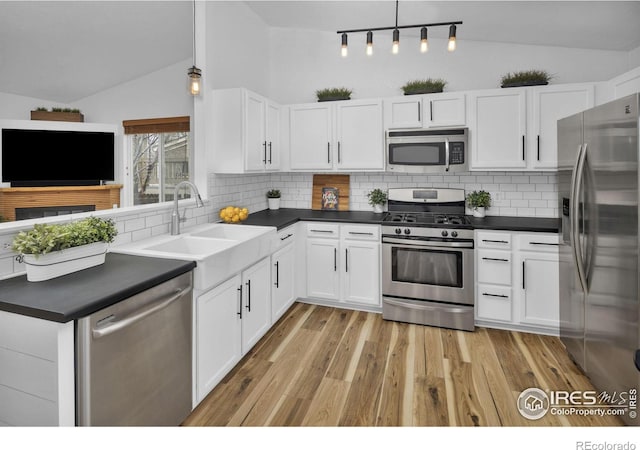 kitchen with lofted ceiling, dark countertops, appliances with stainless steel finishes, and a sink