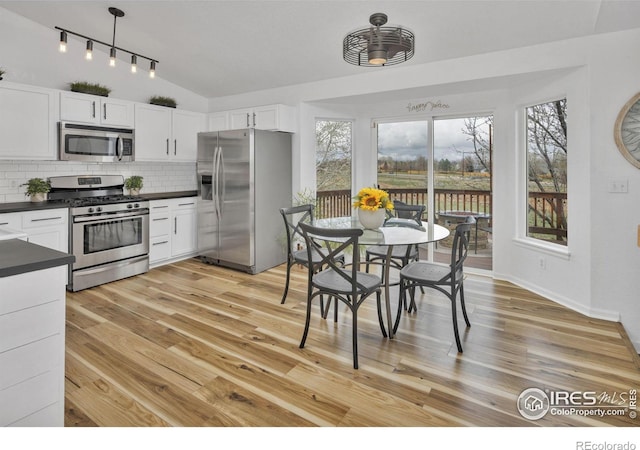 kitchen with tasteful backsplash, dark countertops, lofted ceiling, appliances with stainless steel finishes, and white cabinetry