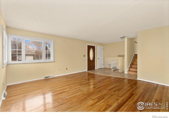 unfurnished living room with stairs, a textured ceiling, wood finished floors, and visible vents