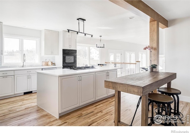 kitchen featuring a kitchen island, light countertops, light wood-type flooring, a sink, and black oven