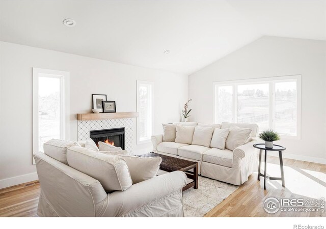 living area featuring a tiled fireplace, baseboards, vaulted ceiling, and light wood finished floors