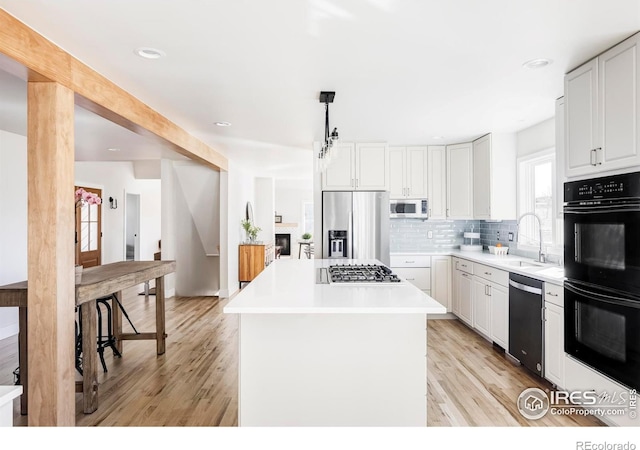 kitchen with stainless steel appliances, a kitchen island, a sink, light wood-style floors, and decorative backsplash