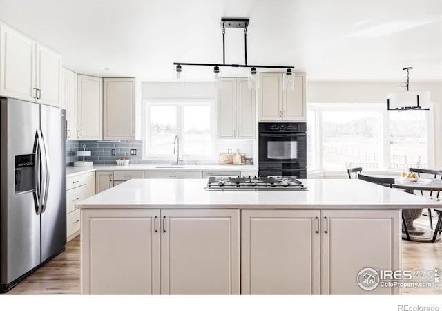 kitchen with a center island, tasteful backsplash, light countertops, appliances with stainless steel finishes, and a sink