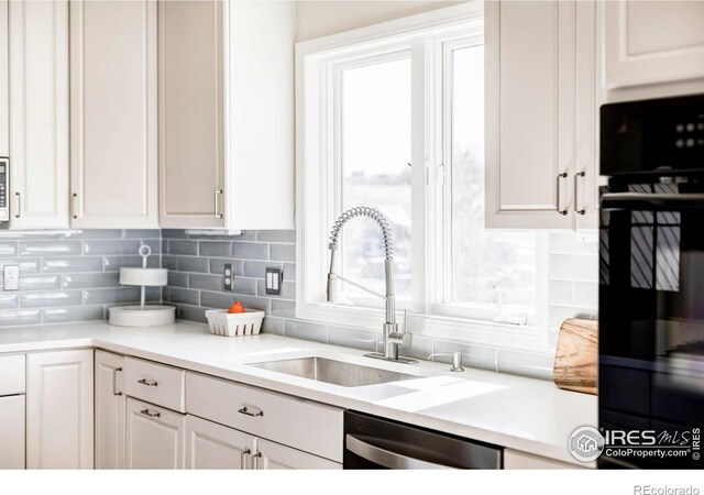 kitchen featuring backsplash, stainless steel dishwasher, white cabinetry, a sink, and oven