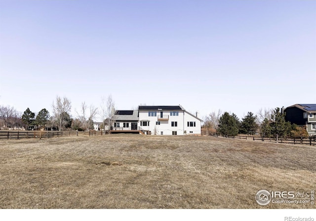 modern farmhouse with roof mounted solar panels, fence, a deck, and a rural view