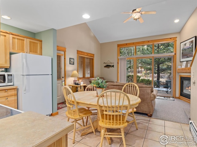 dining room featuring light tile patterned floors, baseboard heating, vaulted ceiling, and a glass covered fireplace