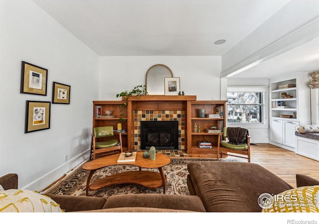 living room featuring built in shelves, a fireplace, baseboards, and wood finished floors