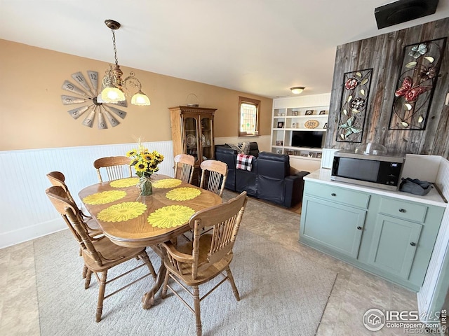 dining space featuring a wainscoted wall, an inviting chandelier, and built in features