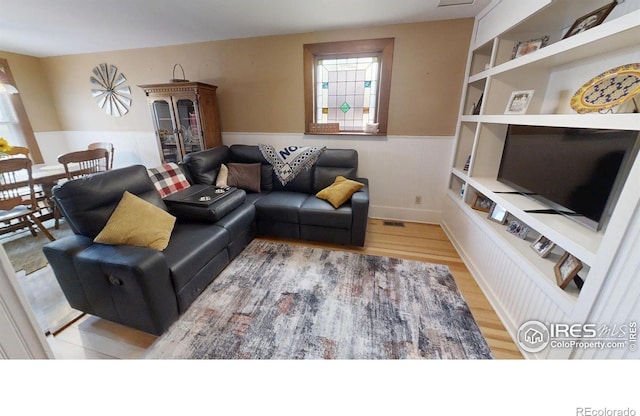 living area featuring a wainscoted wall, visible vents, and wood finished floors