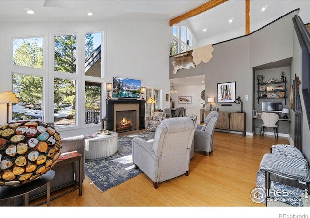 living area featuring a warm lit fireplace, light wood-style flooring, beam ceiling, and a wealth of natural light