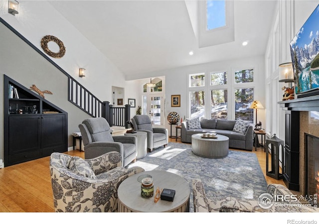 living area featuring high vaulted ceiling, light wood-type flooring, a fireplace, and stairs