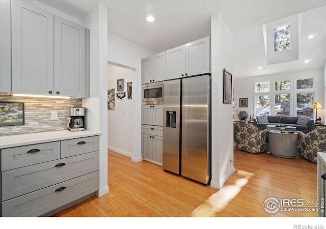 kitchen featuring open floor plan, appliances with stainless steel finishes, light wood-style flooring, and tasteful backsplash