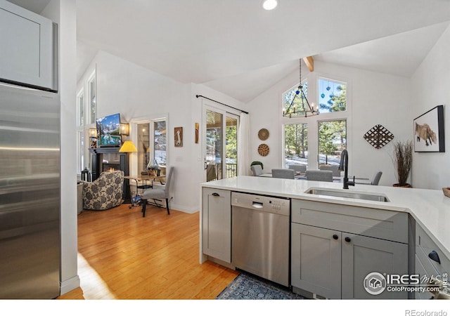 kitchen featuring lofted ceiling with beams, a sink, a lit fireplace, appliances with stainless steel finishes, and gray cabinets