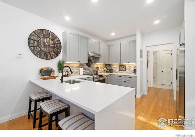 kitchen featuring electric stove, a breakfast bar area, a peninsula, under cabinet range hood, and a sink