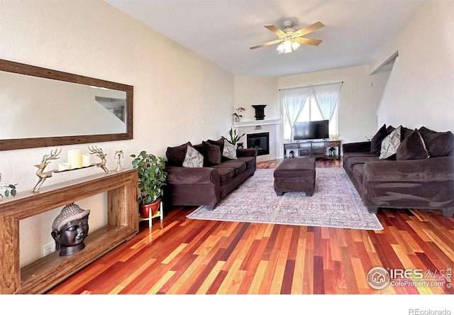 living area featuring a glass covered fireplace, light wood-style flooring, and a ceiling fan