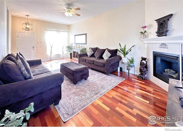 living area with ceiling fan with notable chandelier, a tile fireplace, and wood finished floors