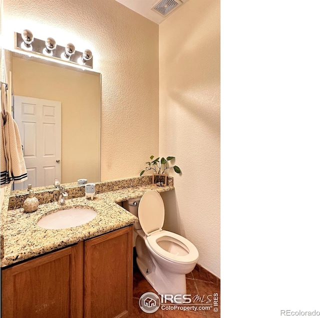 bathroom featuring visible vents, a textured wall, toilet, tile patterned flooring, and vanity