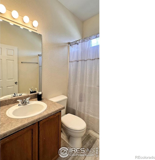 full bathroom featuring a textured wall, curtained shower, toilet, wood finished floors, and vanity