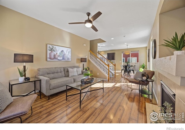 living room featuring ceiling fan, stairs, a fireplace, and wood finished floors