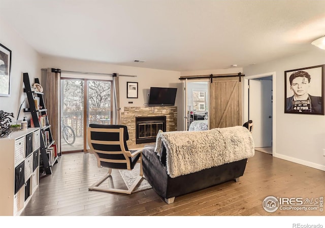 living room featuring a barn door, a fireplace, wood finished floors, visible vents, and baseboards