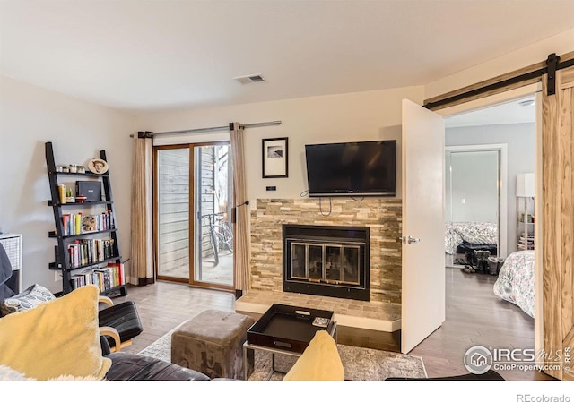 living area featuring a barn door, visible vents, wood finished floors, and a glass covered fireplace