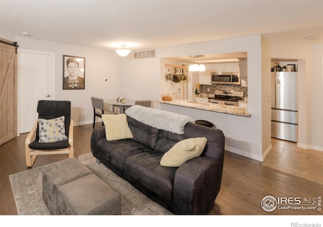 living area featuring baseboards, visible vents, light wood finished floors, and a barn door