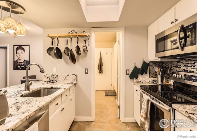 kitchen featuring stainless steel appliances, a sink, baseboards, white cabinets, and decorative backsplash