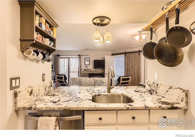 kitchen with a barn door, light stone counters, decorative light fixtures, open shelves, and a sink