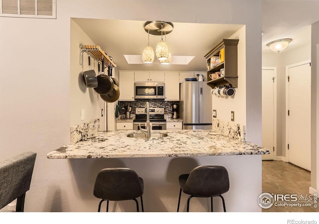 kitchen featuring a skylight, open shelves, tasteful backsplash, appliances with stainless steel finishes, and a peninsula